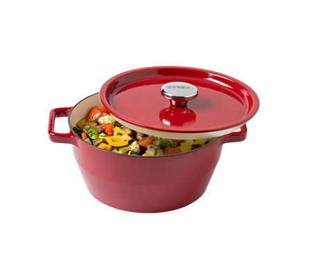 Red enameled cast iron Dutch oven with a lid filled with vegetables on a white background